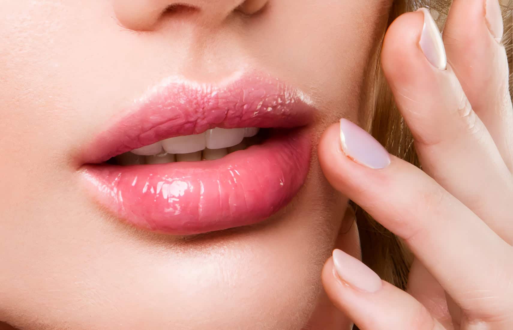 Close-up of a woman's lips with pink lipstick and manicured nails with white tips, showcasing cosmetic beauty treatment results.