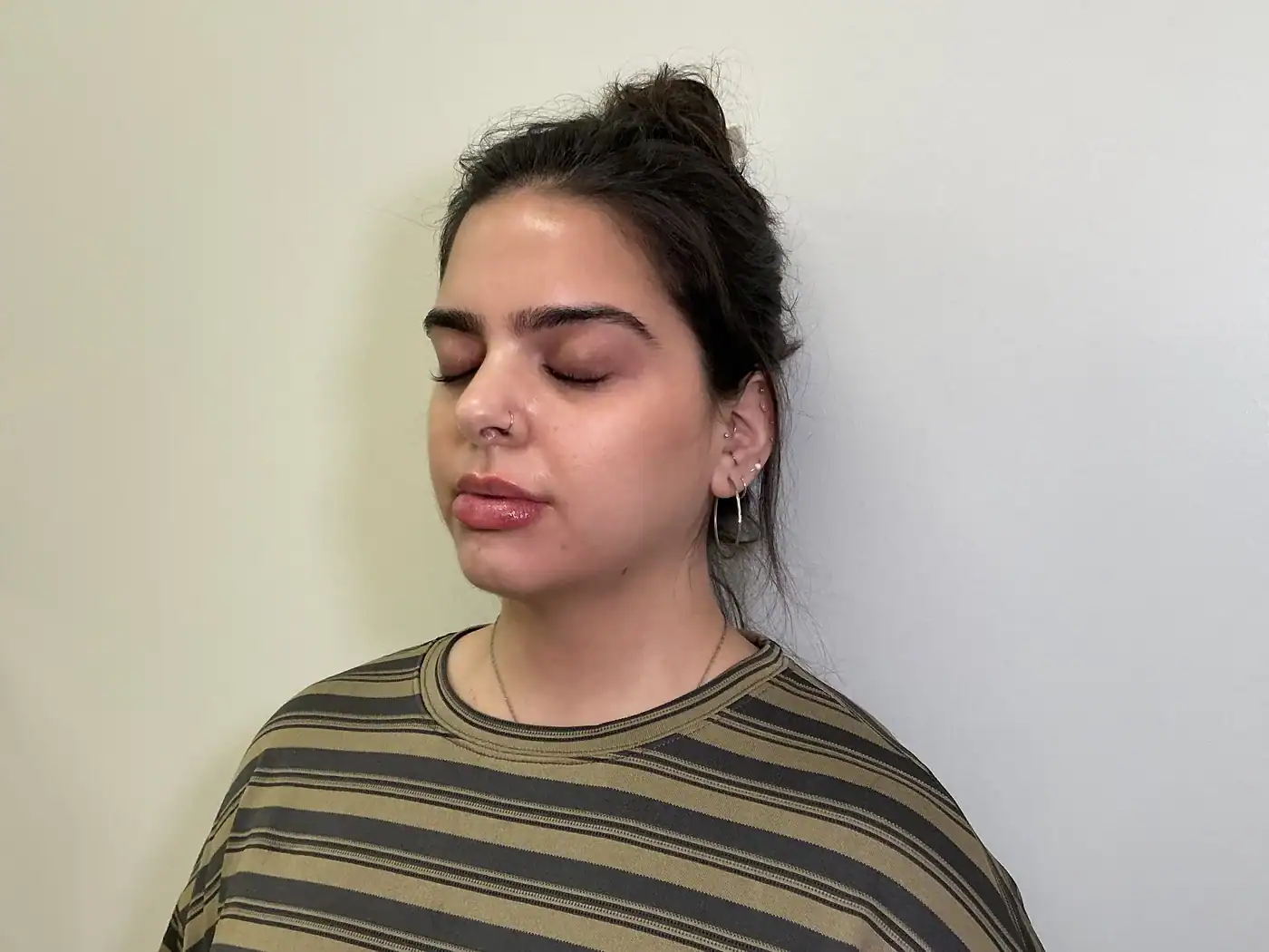 Young woman with dark hair in a bun, eyes closed, in a striped shirt.