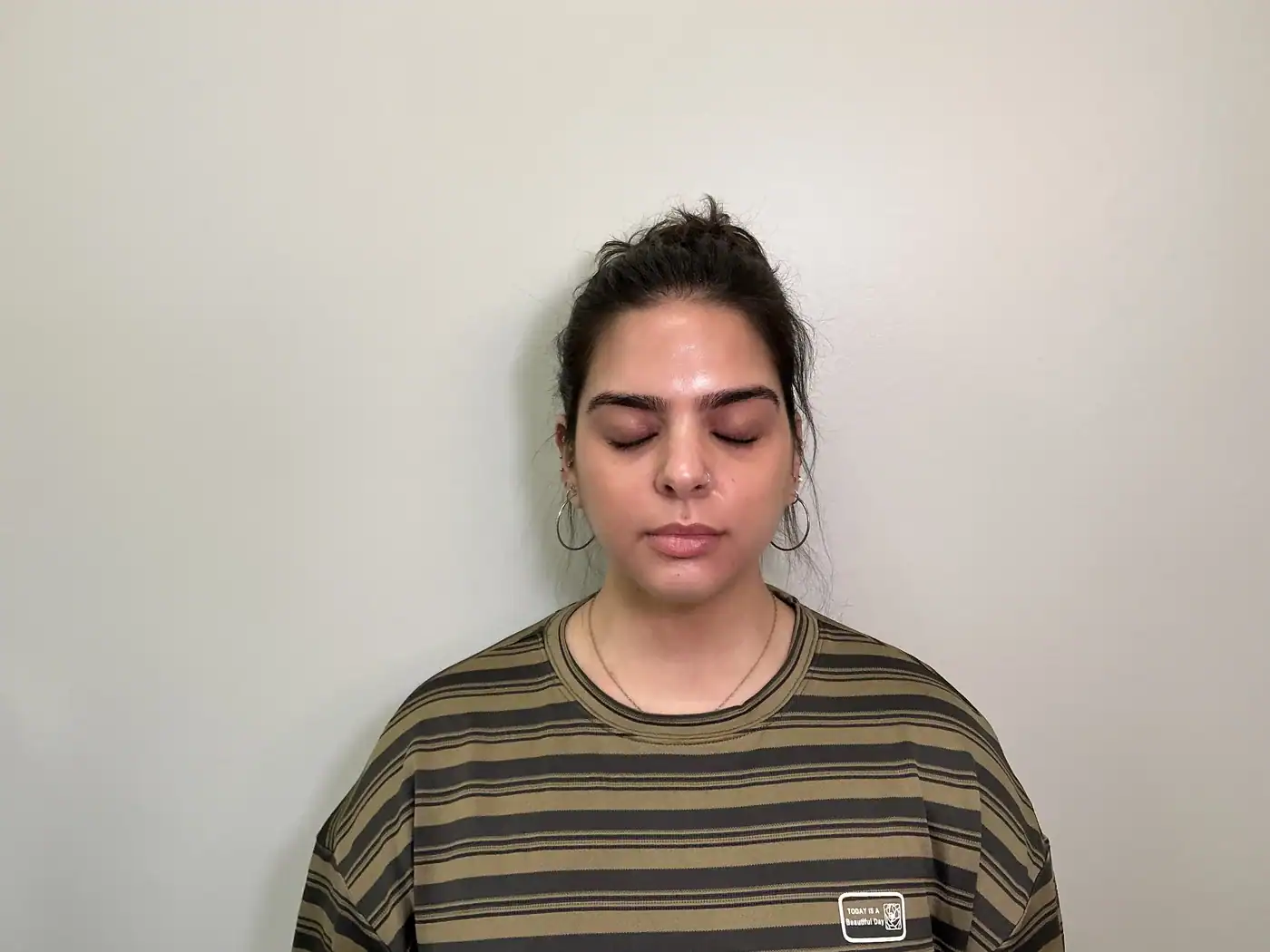 Woman with dark hair in a bun, wearing a striped shirt, with closed eyes and a calm expression.